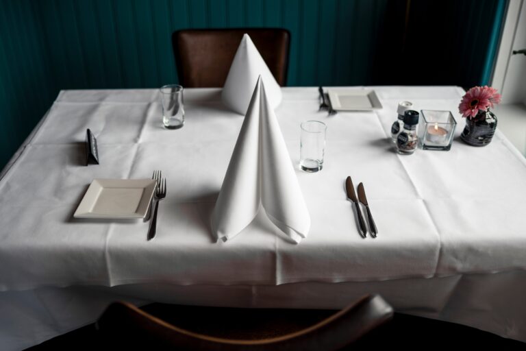 A table set with white linens and sail fold napkin. Elevate your table linens with Stamford Uniform and Linen.