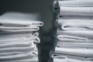 A stack of white linens. Elevate your table linens and uniforms with Stamford Uniform and Linen.