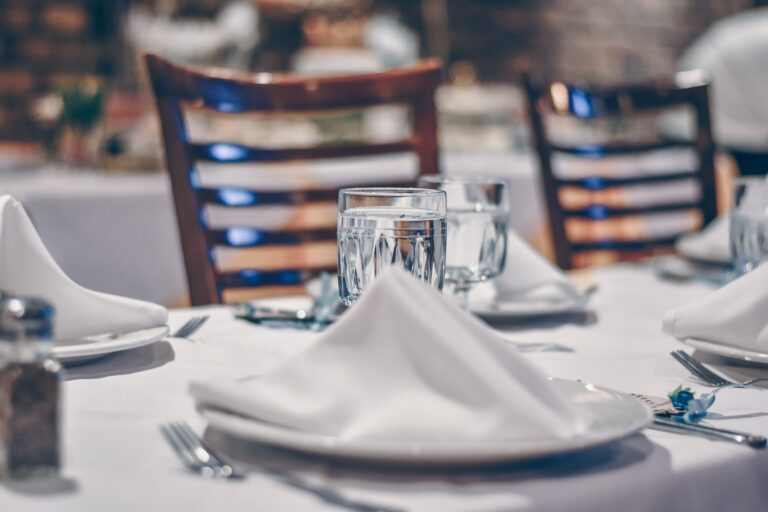 A table set with white linens and sail fold napkin. Elevate your table linens with Stamford Uniform and Linen.