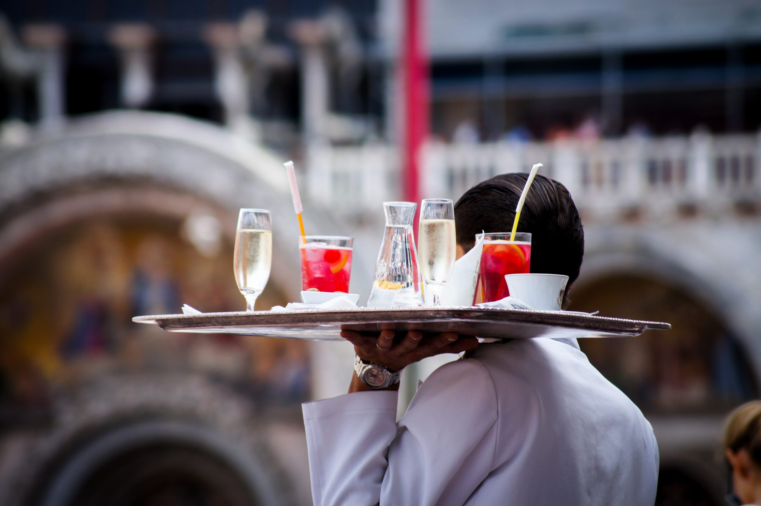 A waiter carries a tray of drinks. Elevate your staff with custom uniforms from Stamford Uniform and Linen.