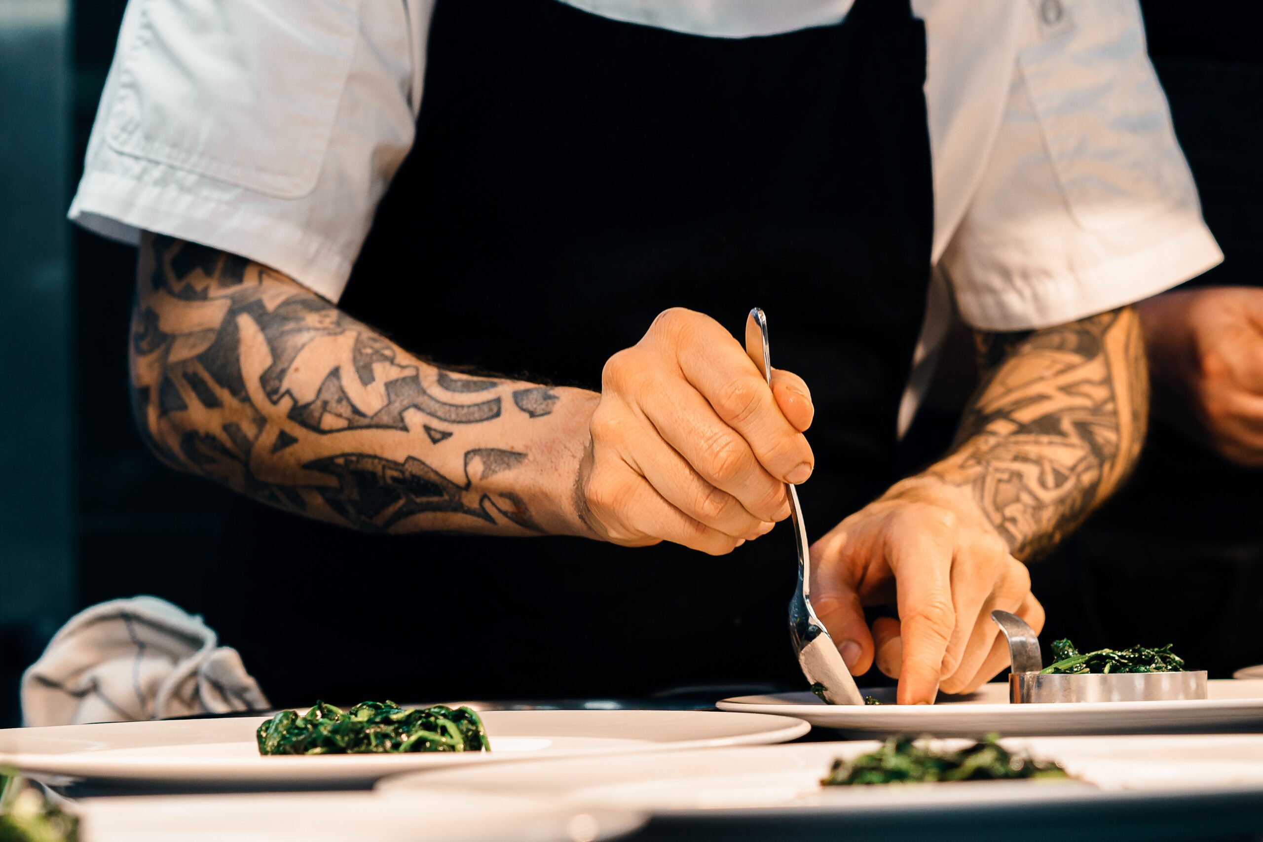 A chef in a black apron plates a dish. Elevate your staff with custom uniforms from Stamford Uniform and Linen.